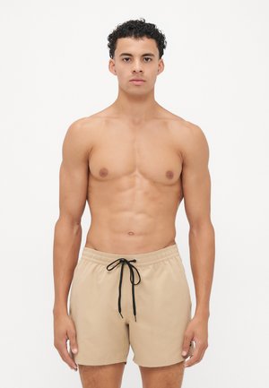 Beige badedraktshorts med elastisk livlinje og svart snor. Glatt tekstur og rett snittdesign, egnet for strandklær.