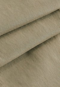 Bomuldsstof i en dæmpet grøn-beige farve, med en fin ribbet tekstur og synlige sømme langs kanterne.