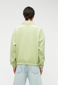 Ανοιχτό πράσινο φούτερ με γιακά, ραβδωτές μανσέτες και μέση. Λείος υφάσματος. Έχει κεντημένο λογότυπο στο πίσω μέρος.