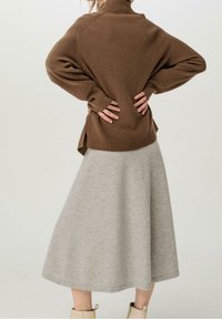 Pull marron côtelé avec un col montant, associé à une jupe grise évasée. La tenue présente une coupe ample et une texture douce.