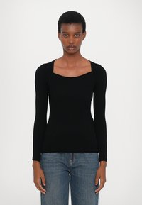 Svart ribbestrikket langermet topp med firkantet utringning og tettsittende silhuett, kombinert med lys blå denimjeans. Teksturert stoff og formtilpasset design.