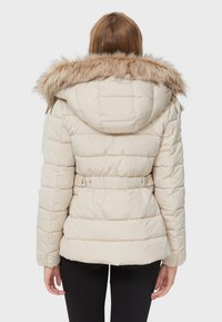 Beige pufferjakke med en aftagelig faux fur hætte, quiltet design, justerbart bælte i taljen og elastiske manchetter.