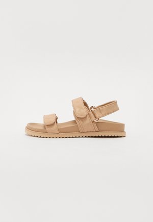 Tan sandals with adjustable Velcro straps, quilted design, flat rubber sole, and a zigzag edge. Suitable for casual wear.