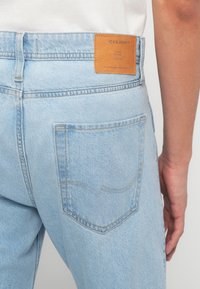 Ανοιχτό μπλε τζιν denim από πίσω, που δείχνει μια τσέπη και ένα καφέ δερμάτινο ετικέτα της μάρκας Jack & Jones κοντά στη μέση.