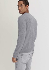 Grauer Strickpullover mit Rundhalsausschnitt, taillierten langen Ärmeln und geripptem Saum. Kombiniert mit hellgrauen Jeans. Lässiges Design.