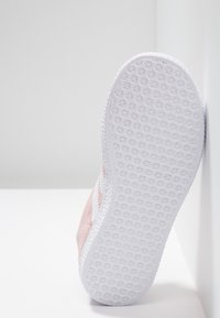 Ljusrosa mockasneakers med en vit gummisula, som har ett texturerat greppmönster och en ren, minimalistisk design.
