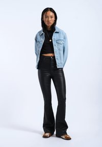 Lichtblauwe denimjas over een zwarte cropped top, hoge zwarte flared pants en gemusterde schoenen. Gladde texturen en contrasterende kleuren.