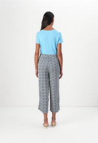 Top azzurro chiaro a maniche corte abbinato a pantaloni larghi a navi e bianchi con un design geometrico. Sandali con tacco semplici.