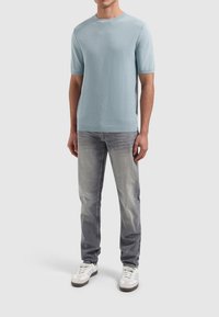 Lichtblauwe gebreide trui met korte mouwen en een textuurpatroon, gecombineerd met vervaagde grijze jeans en witte sneakers met grijze accenten.