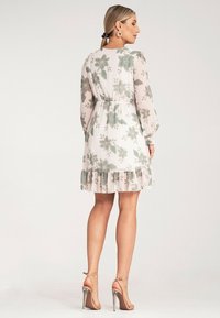 Sukienka w kwiatowy wzór, wykonana z lekkiego materiału, z zaznaczoną talią, długimi rękawami i falbaniastym dołem w pastelowych kolorach z zielonymi akcentami.