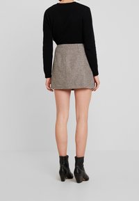 Svart tröja och en kort brun houndstooth kjol med fransad fåll. Modellen bär svarta klackade ankelstövlar. Neutral grå bakgrund.