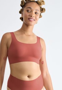 Roestkleurige bralette en bijpassende hoge slip gemaakt van gladde stof, met brede bandjes en een minimalistisch ontwerp.