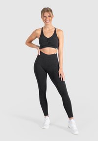 Zwart sportoutfit met een cropped tanktop met een geplooide voorkant en hoge taille leggings. Gemaakt van rekbaar, gestructureerd materiaal.