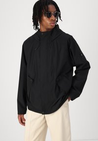 Schwarze, wasserdichte Jacke mit Kapuze, verschließbarem Vorderteil und seitlichen Taschen. Sie zeichnet sich durch eine elegante, glatte Textur und eine lockere Passform aus.