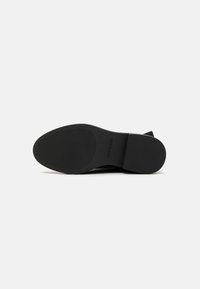 Talpa de încălțăminte neagră din cauciuc texturat, cu șanțuri orizontale pentru aderență și un design minimalist. Branding vizibil pe lateral.