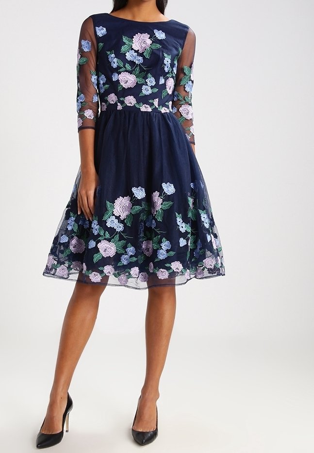 Navy blauwe jurk met doorschijnende lange mouwen, versierd met kleurrijke bloemenborduursels, een aansluitend lijfje en een uitlopende rok met een zoom boven de knie.