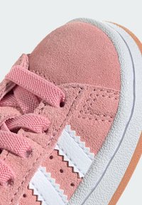Ružové semišové tenisky s textilnými šnúrkami, bielymi koženými pruhmi so zigzagovými okrajmi, štruktúrovanou gumenou podrážkou a detailným prešívaním.