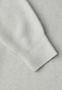 Tela de suéter gris claro con una textura suave. Vista en primer plano del detalle del puño acanalado, que muestra su patrón de tejido y acabado de puntadas.