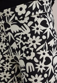 Fekete leggings, fehér virágmintával, különböző virágformákkal és díszítésekkel. Simaság jellemzi, rugalmas derékkal.