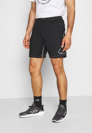 Zwarte sportshorts met een taillekoord, zijzakken en contrasterende witte stiksels. Gecombineerd met donkergrijze sneakers en zwarte sokken.