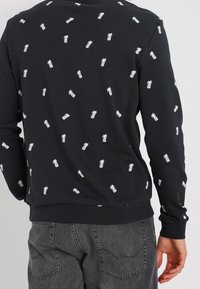 Czarna bluza z białym nadrukiem w ananasy, żeberkowe mankiety i dół, okrągły dekolt, teksturowany materiał, luźny krój, casualowy design.