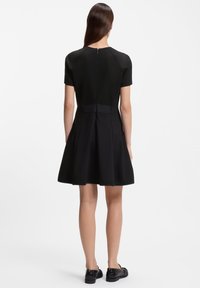 Μαύρο φόρεμα με κοντά μανίκια, στενή εφαρμογή στο μπροστινό μέρος και φουσκωτή φούστα, με κλείσιμο φερμουάρ στο πίσω μέρος και λεία υφή.