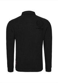 Svart långärmad pikétröja i bomull med krage, logga på ryggen och sidospjäll för en avslappnad passform.