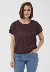 Burgunderfarbendes und schwarzes, floral gemustertes kurzärmliges Oberteil, rundhals, leichtes Material, lockere Passform, getragen mit blauen Jeans.