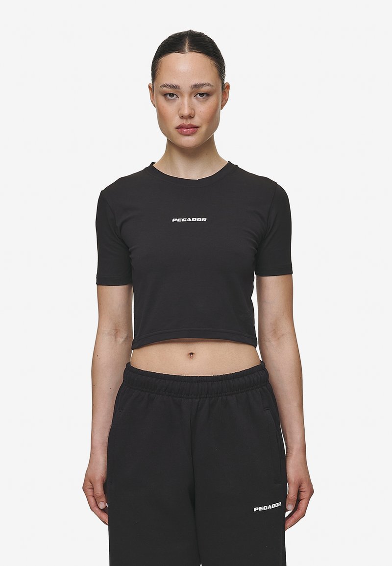 Černé cropped tričko vyrobené z lehkého materiálu, s kulatým výstřihem a krátkými rukávy, s bílým logem "PEGADOR" na přední straně.