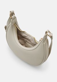 Beżowa skórzana torebka o zaokrąglonym kształcie, z zamkiem błyskawicznym w kolorze złota i wewnętrzną kieszenią. Posiada krótki pasek z elementami ozdobnymi w kolorze złota.