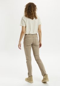 Pantalones beige ajustados con bolsillos traseros, vistiendo una camiseta gris claro, combinados con botas beige hasta el tobillo, vistos desde atrás.
