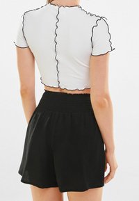 Vit ribbad crop top med svarta volanger i kanterna och korta ärmar, tillsammans med svarta shorts med smockat midjeband. Texturerad tyg, figuret fitting design.