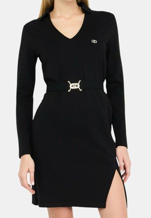Czarna sukienka z długim rękawem, dekoltem w serek, złotą klamrą paska, małym logo na piersi oraz rozcięciem do uda po prawej stronie.