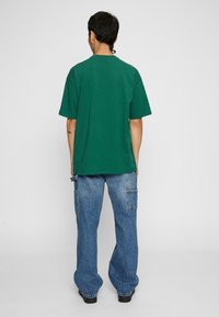 Groene katoenen t-shirt met een klassieke pasvorm, korte mouwen en een ronde hals, gecombineerd met blauwe wijde spijkerbroeken met zijzakken.