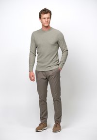 Maglione grigio con texture e scollo rotondo, abbinato a chinos marrone chiaro e sneakers marroni. L'outfit è casual e aderente.