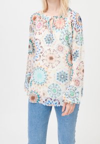 Blouse fluide à motifs en tissu léger présentant un design kaléidoscopique avec des motifs circulaires en bleu, rose et vert ; détail noué au niveau de l'encolure.