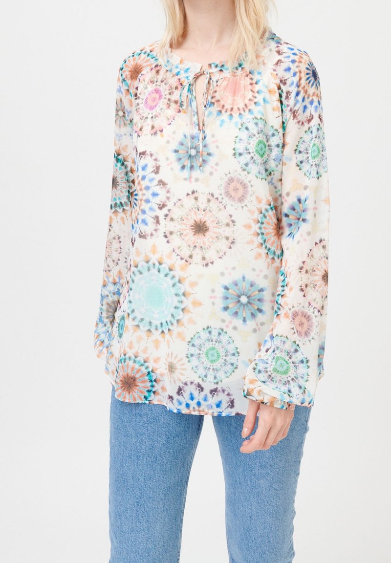 Blouse fluide à motifs en tissu léger présentant un design kaléidoscopique avec des motifs circulaires en bleu, rose et vert ; détail noué au niveau de l'encolure.
