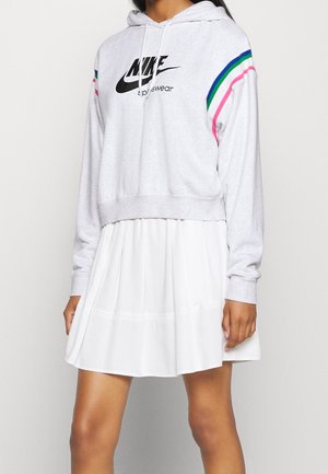 Osoba nosząca jasno szarą bluzę sportową Nike z kapturem z niebieskimi i różowymi paskami na rękawach, w połączeniu z białą plisowaną spódnicą.
