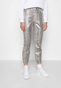 Metalliska silverbyxor med ett ormskinnsmönster, slim fit, cropped längd; i kombination med vita sneakers och strumpor som når ankeln.