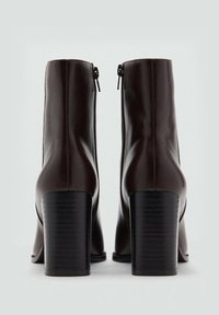 Braune Stiefeletten aus Leder mit glatter Oberfläche, Reißverschluss an der Rückseite und robusten schwarzen Blockabsätzen. Das Design zeichnet sich durch eine schlanke Silhouette aus.