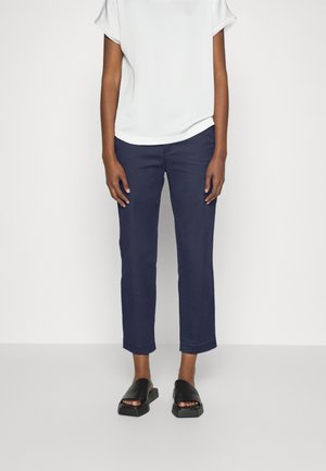 Pantalones de algodón azul marino con corte recto y dobladillos recogidos, combinados con una blusa blanca de manga corta y sandalias negras tipo deslizamento.