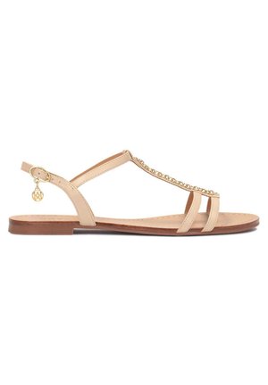 Sandale plate beige avec fines lanières, détail chaîne dorée sur le dessus et petit charme doré accroché à la bride de la boucle à la cheville.