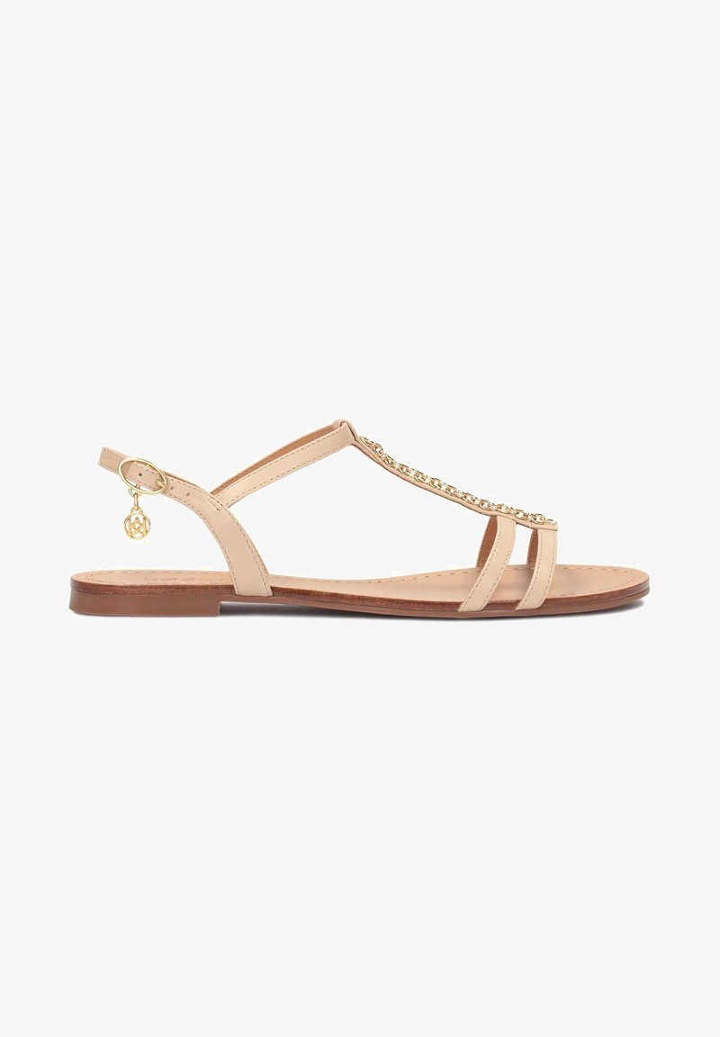 Sandale plate beige avec fines lanières, détail chaîne dorée sur le dessus et petit charme doré accroché à la bride de la boucle à la cheville.