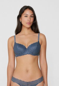 Dunkelblaßer Spitzen-BH mit Bügelunterstützung, verstellbaren Trägern, gewellten Kanten und Blumenmuster. Passende Spitzenunterhosen sichtbar.