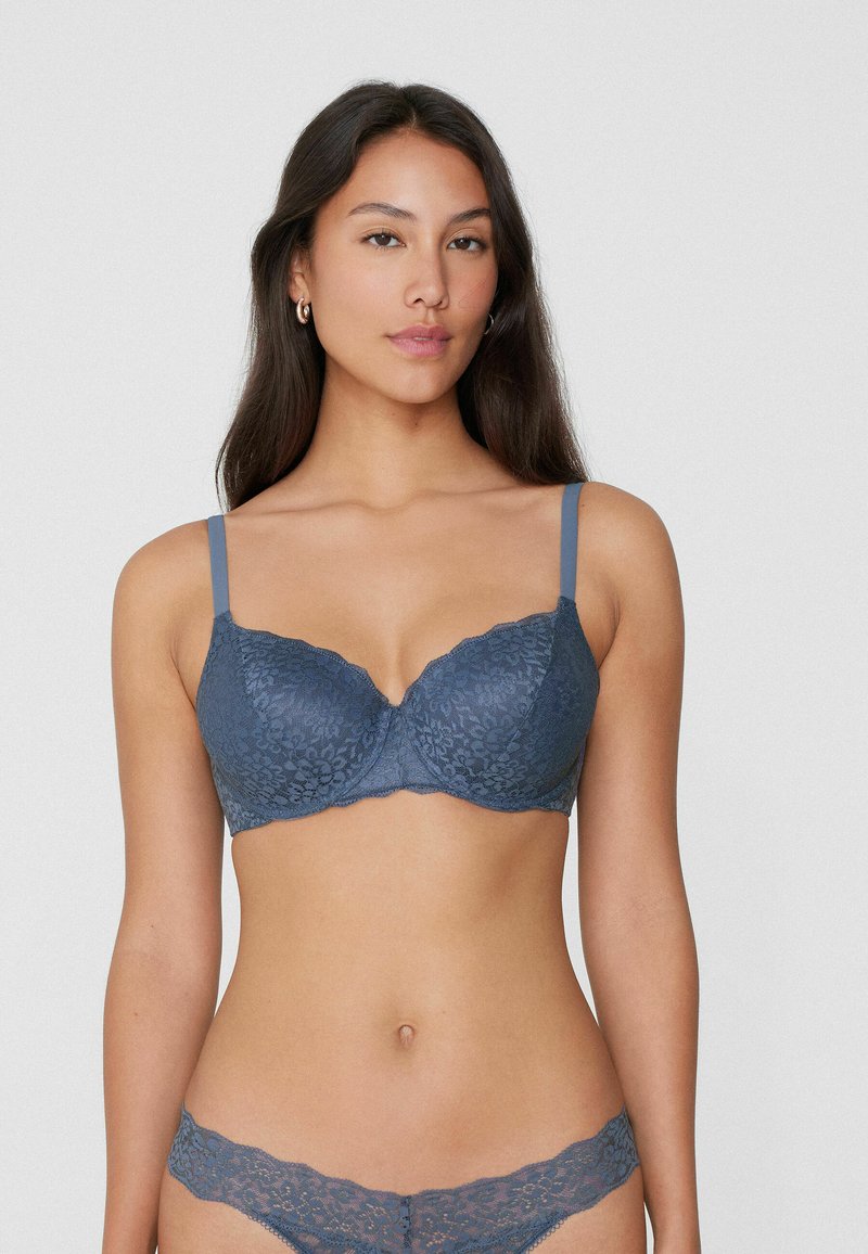 Dunkelblaßer Spitzen-BH mit Bügelunterstützung, verstellbaren Trägern, gewellten Kanten und Blumenmuster. Passende Spitzenunterhosen sichtbar.