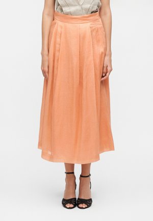 Donna che indossa una gonna midi a vita alta color pesca con pieghe, abbinata a tacchi neri con punta aperta e cinturino alla caviglia su uno sfondo semplice.