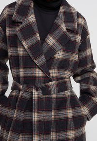 Abrigo a cuadros hecho de mezcla de lana, con un esquema de colores en gris oscuro, beige y rojo, con cinturón en la cintura y solapas anchas.