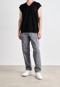 Czarny dzianinowy sweter bez rękawów z dekoltem w serek, w połączeniu z jasnoszarymi spodniami i białymi trampkami, tworzy prostą, nowoczesną stylizacj ę.