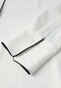 Hvid skjorte stof med sort piping langs kraven. Kraven har en knapdetalje. Glat tekstur og klassiske designelementer.