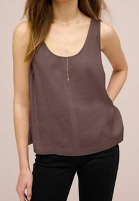 Haut sans manches couleur marron avec encolure dégagée, coupe décontractée, texture douce, associé à un collier en argent à plusieurs rangs, sur un fond neutre.